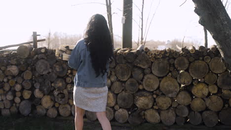 Rear-view-of-caucasian-woman-piling-up-firewood-outside-a-country-house