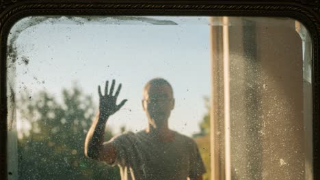 a solitary figure stands outside a window, reaching out with a hand against a dusty glass surface, creating an evocative moment that captures longing and isolation