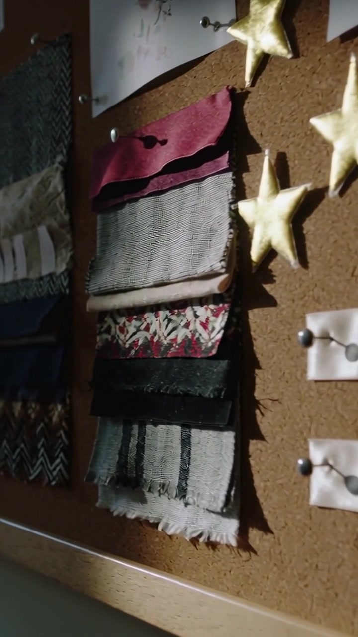 Vertical video: Panning camera left over corkboard wall showing fabric swatches pins and gold stars
