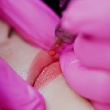 lips tattoo. cosmetologist in pink gloves applying permanent makeup tattoo on lips. professional tattooist making permanent make up. close-up.