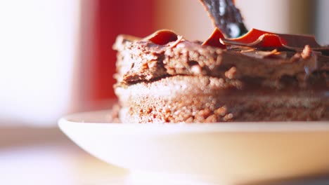 slow motion of hand using knife cutting into sweet delicious soft chocolate fudge cake in kitchen setting with natural lighting. close up food photography footage.