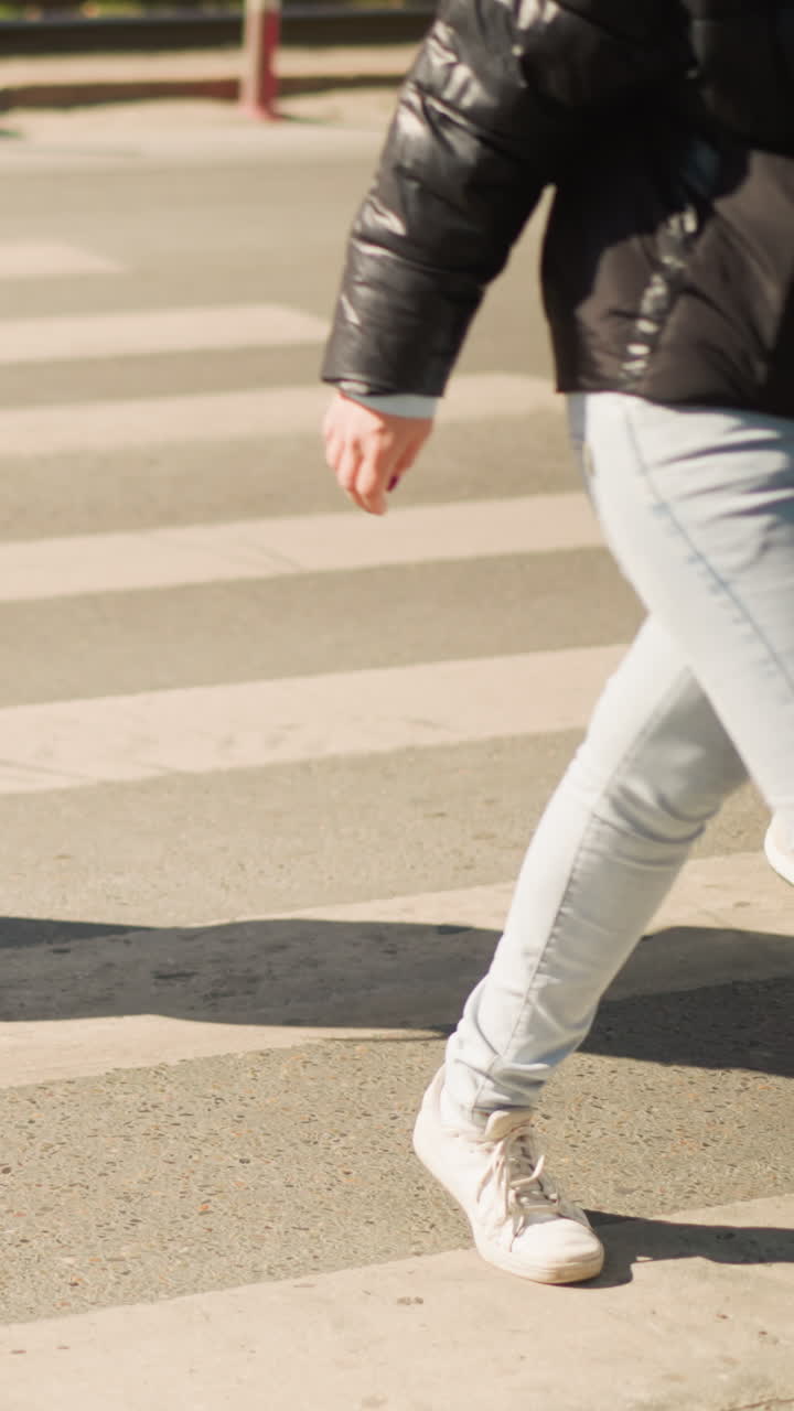 pedestrians crossing zebra crosswalk in sunlight, family members and commuters moving across striped pavement, child holding hand, adult carrying bag and headphones, casual sneakers and jeans, warm