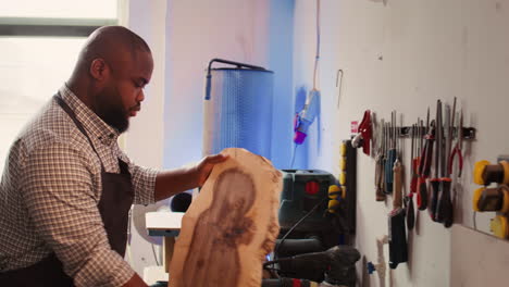ebanista en el estudio de carpintería evaluando el bloque de madera, comprobando si hay daños