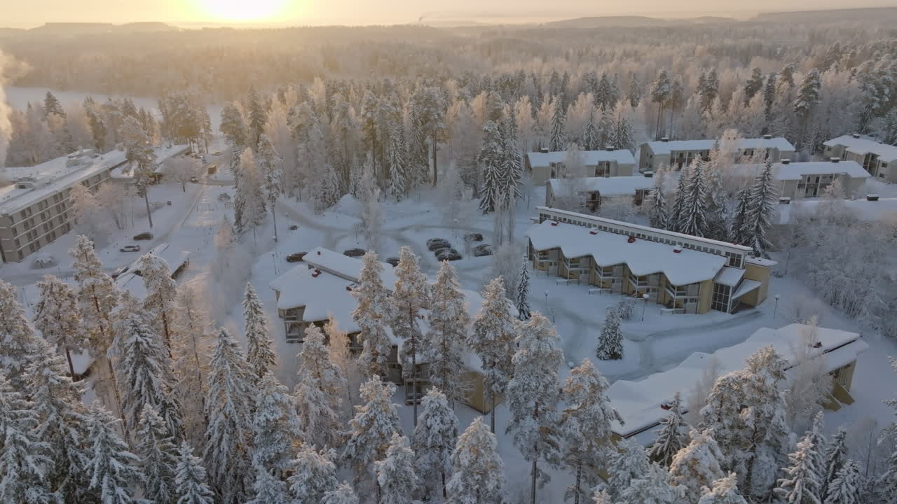 Drone circling apartment buildings surrounded by frosty forest, winter sunrise