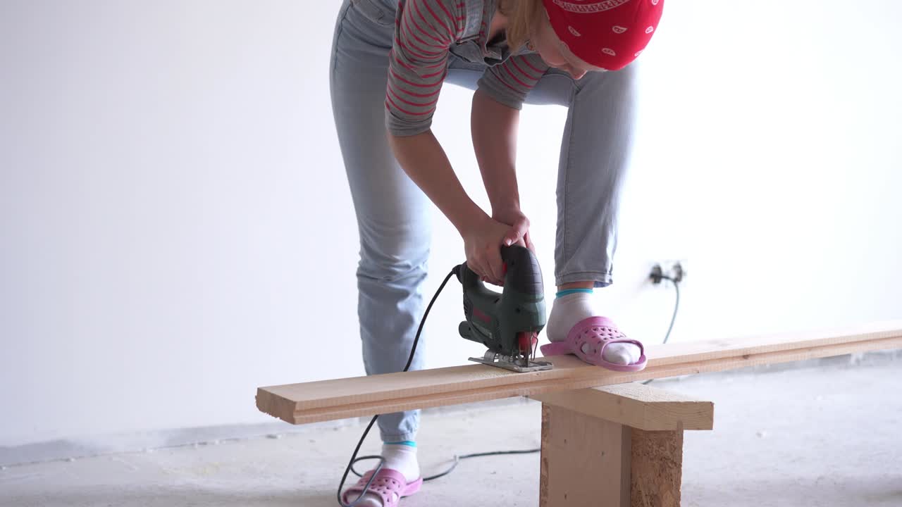 una mujer hace un trabajo no femenino - aserrar una tabla de madera con un rompecabezas eléctrico