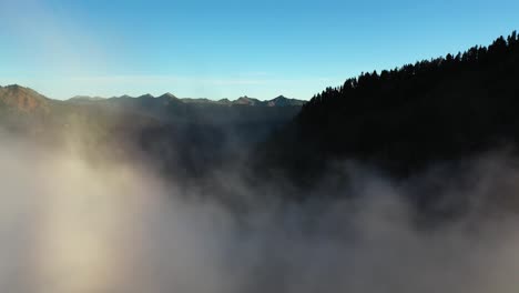 fritando através do nevoeiro acima do vale e da floresta perene sob o céu azul e os picos das montanhas na manhã ensolarada