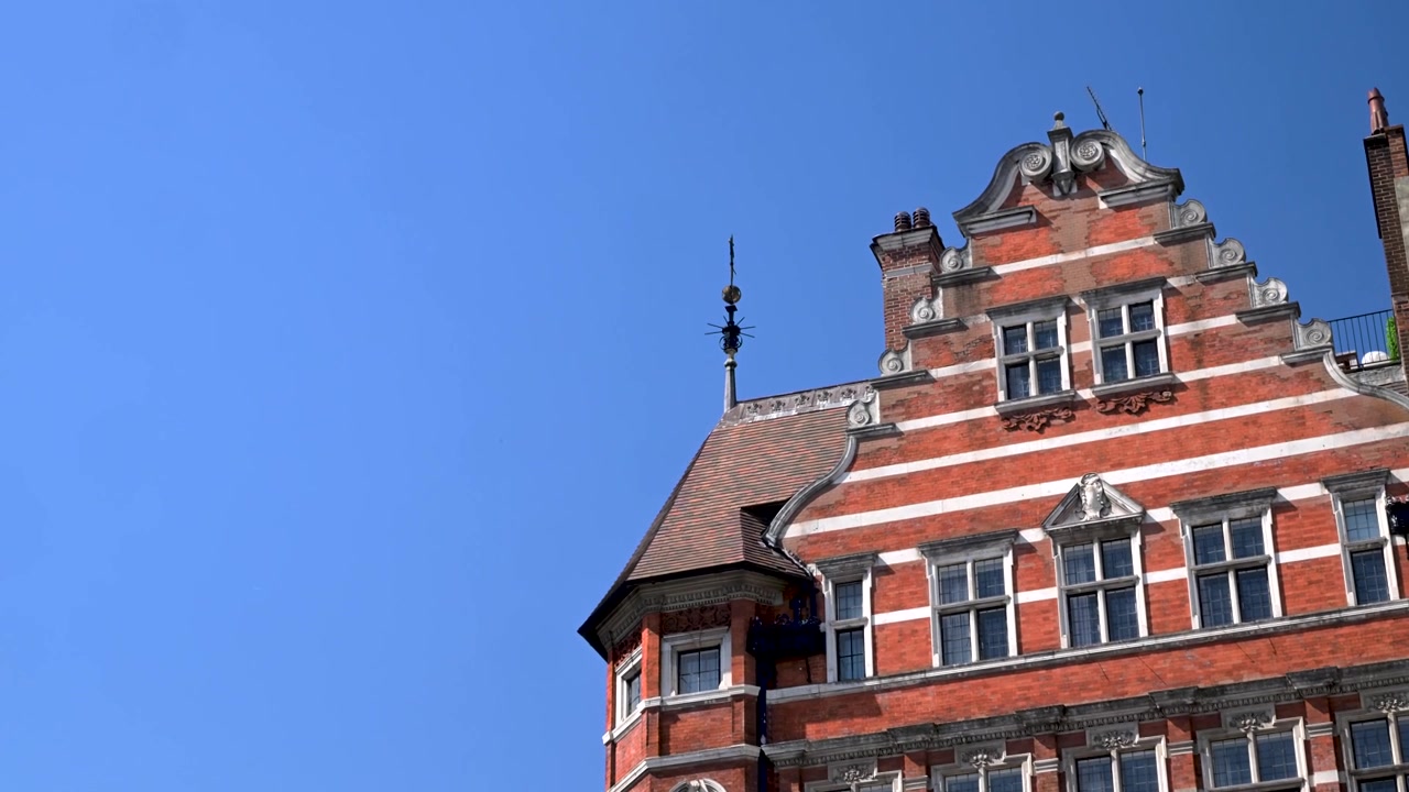 Het bovenaanzicht van een historisch rood bakstenen gebouw met een sierlijk dak in Londen. Toont architectonische details en een heldere hemel. Geweldig voor architectuur- of reisgerelateerde content.