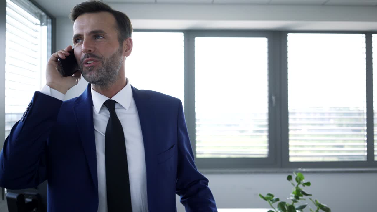 hombre de negocios alegre hablando por teléfono y caminando por la oficina