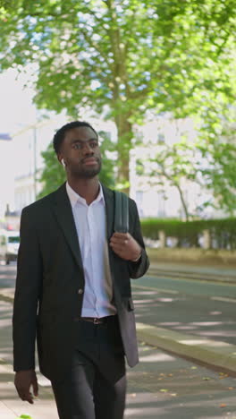 vertical video of young businessman wearing wireless earbuds streaming music or podcast checking mobile phone on walk to work in offices in the financial district of the city of london uk - shot in real time