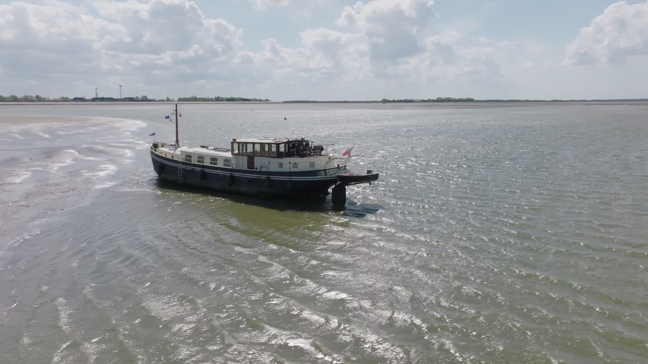 Side profile of a traditional boat beside shallow mudflats; green water in foreground, daylight