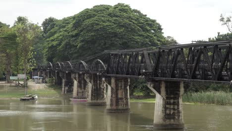 a static shot of the iconic railway bridge over the river kwai, the calm waters of the khwae noi river flows below in kanchanaburi, thailand