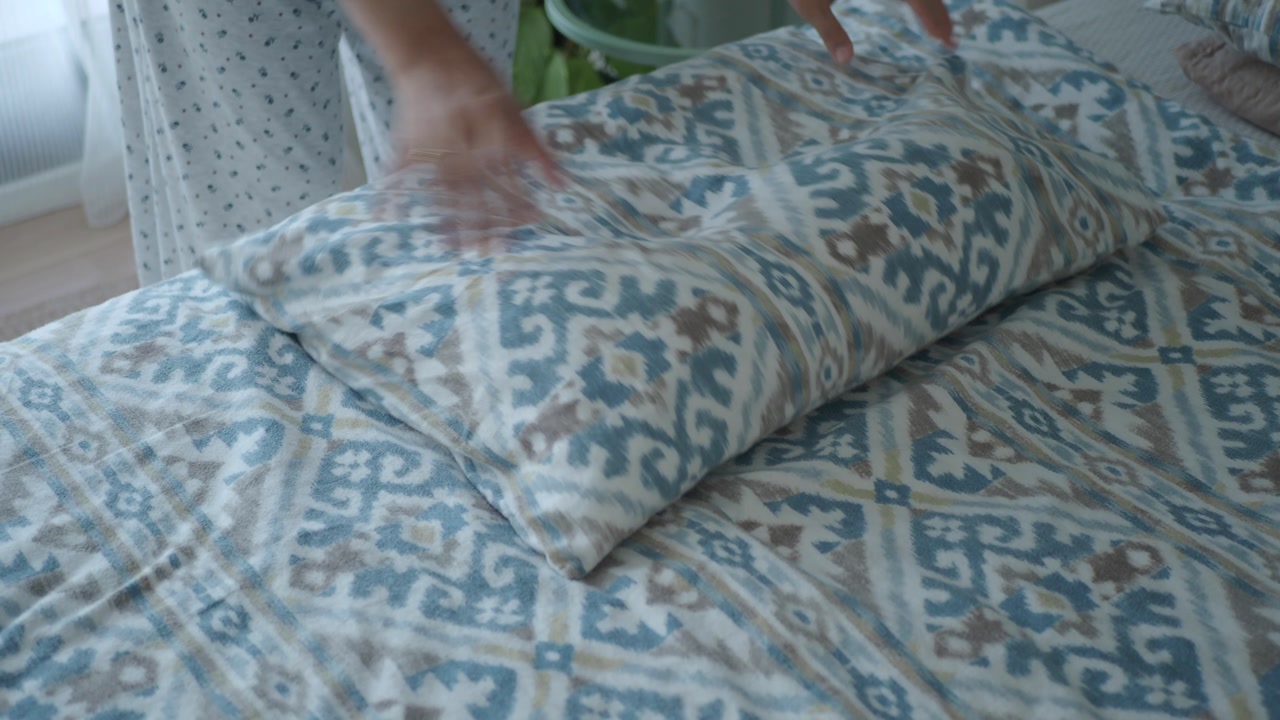 Hands Arranging Pillows on a Patterned Bed