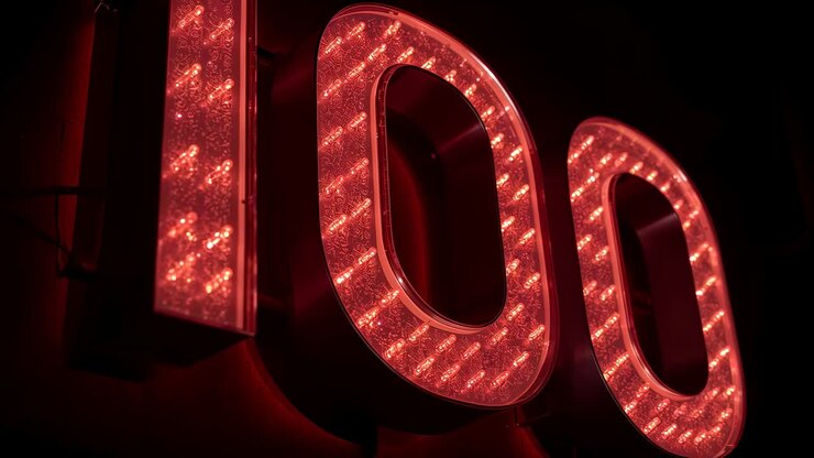 Moving camera sliding right, zooming, revealing red LED 100 sign at dark panel, showing LED texture