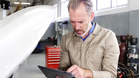 mecánico usando una tableta digital mientras hace servicio a un motor de automóvil
