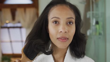 Portrait-of-mixed-race-woman-wearing-bathrobe-brushing-her-hair