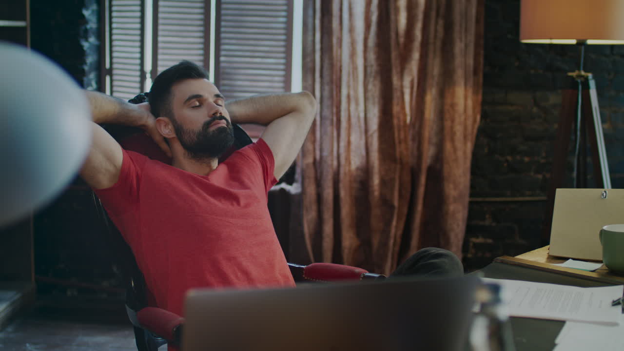 ⁇ 수염 을 가진 사람 이 집 사무실 에서 저녁 에 일 한 후 의자 에서 휴식을 취하고 있다