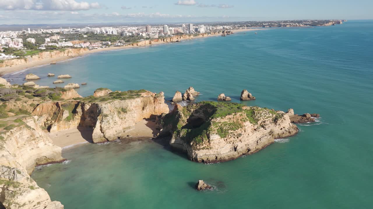 Riprese aeree che sorvolano Ponta João de Arens a Portimão, Algarve, mostrando scogliere spettacolari, una vegetazione lussureggiante e acque di un blu profondo.