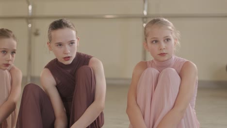 a group of young ballet students in black dancewear practicing positions in a spacious ballet studio with wooden flooring and wall-mounted barres. focused expressions and synchronized movements.