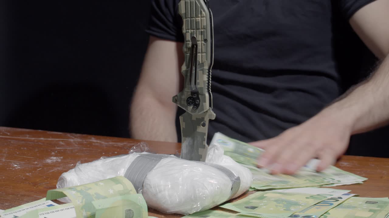 한 남자가 날카로운 칼로 코카인을 찔러 탁자 위에 지폐를 세었다