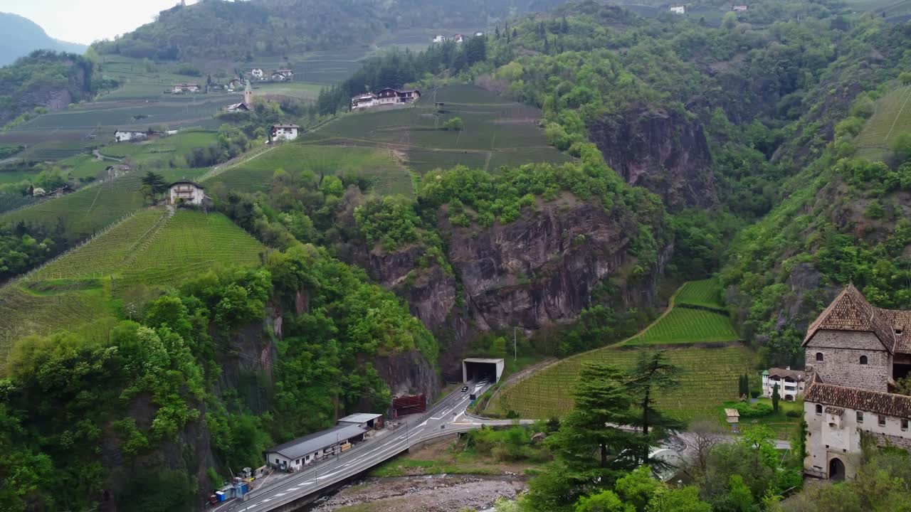 Aerial shot flying around Roncolo Castle with a visible tunnel entrance in the mountain nearby