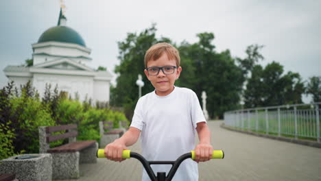 a close-up view of a child riding a scooter on a paved path with a scenic building behind him