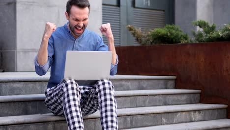 casual man celebrating win on laptop sitting on stairs