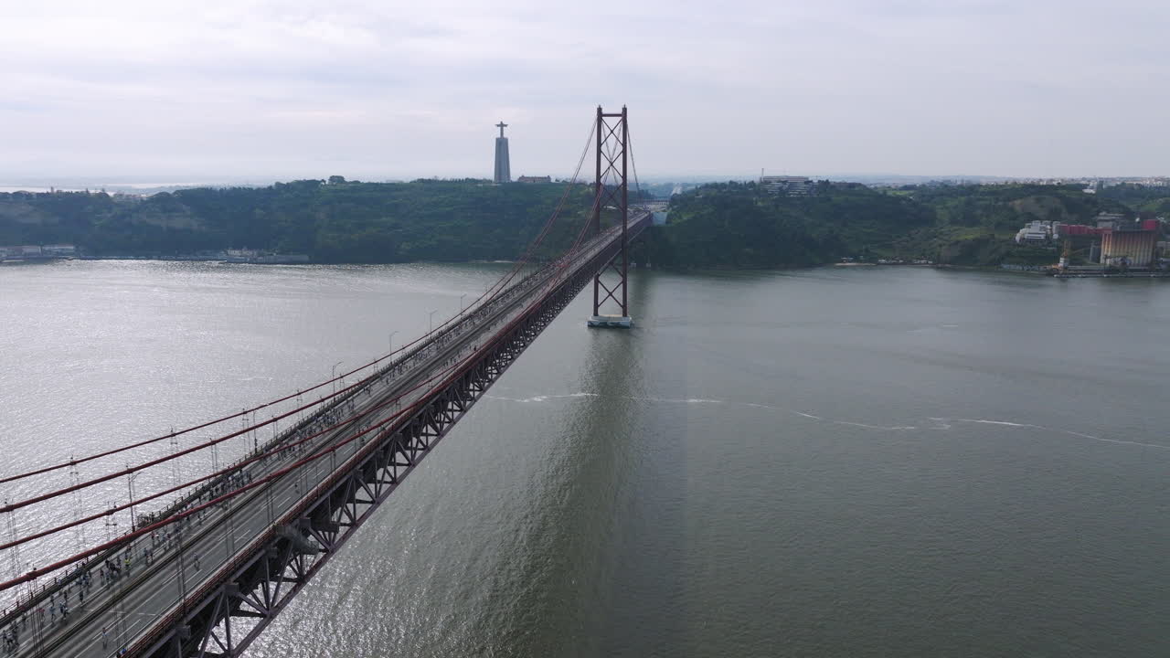 Half marathon and 10K long distance running event in Lisbon, Portugal, Europe. Runners crossing the iconic famous red 25th April suspension bridge by Cristo Rei. Tagus river panorama drone aerial view