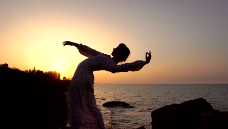 adorable caucasian brunette girl in light dress dancing at the cliff above the sea at sunrise time