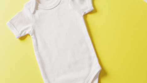 Video-of-close-up-of-white-baby-grow-on-yellow-background