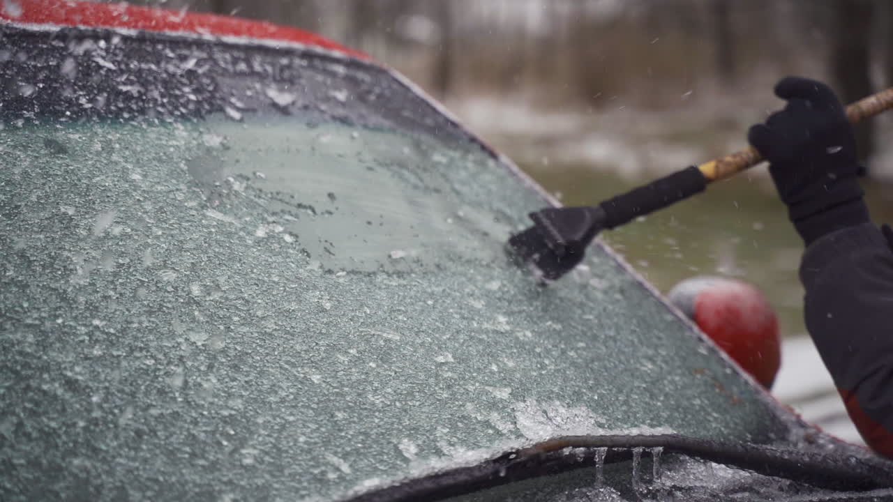 Man cleaning and scraping ice from car windshield in snow