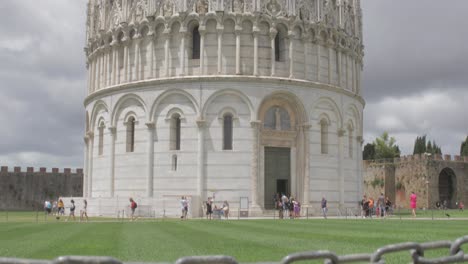 tilt up from a do not walk on grass sign to reveal the popular tourist destination of the pisa baptistery in italy