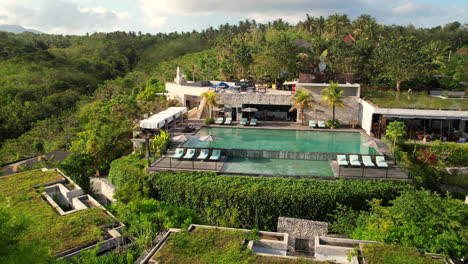 tropical hotel and resort on hilltop with large swimming pool lounge at maua nusa penida, aerial revealing