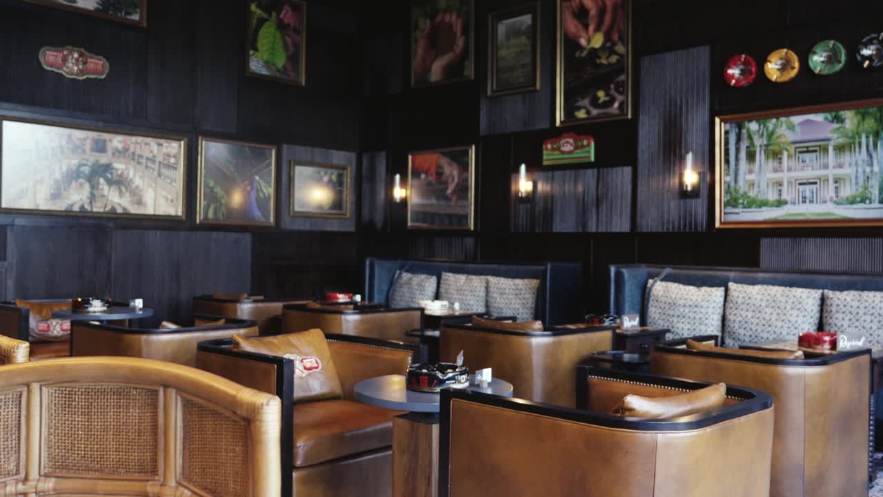 Carrellata all'indietro da un bordo di marmo per rivelare una sofisticata lounge d'hotel caratterizzata da boiserie in legno scuro, poltrone club in pelle e una parete galleria sotto una calda illuminazione ambientale.