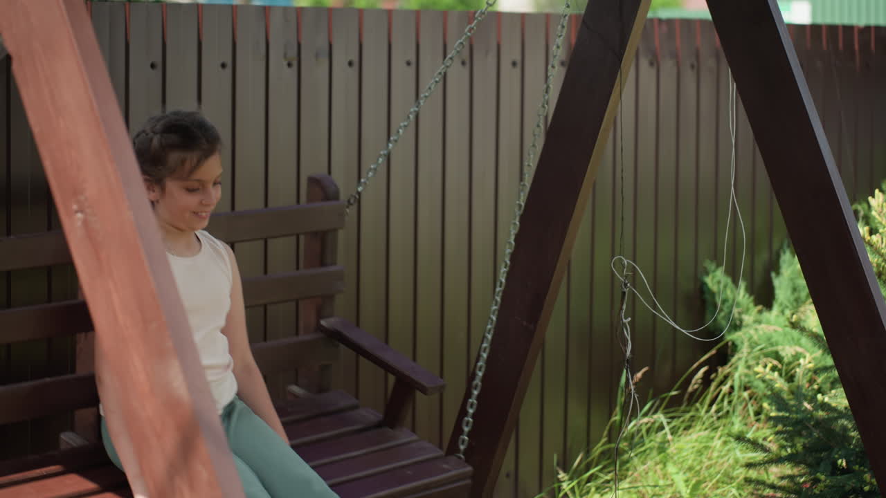Child Swinging Happily, Preteen Smiling Peacefully On Wooden Seat, Joyful Young Girl Lounging On Swing In Sunlight, Happy Preteen Calmly Sitting On Swing Amid Lush Green Surroundings And Sunlight