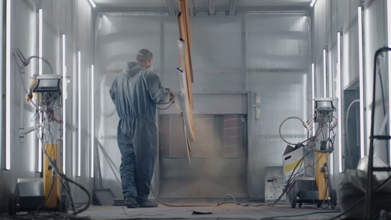 General plan A man in a respirator is painting metal with a powder method. Production of steel and metal structures. Painting shop. The painter works with a spray gun paint is applied