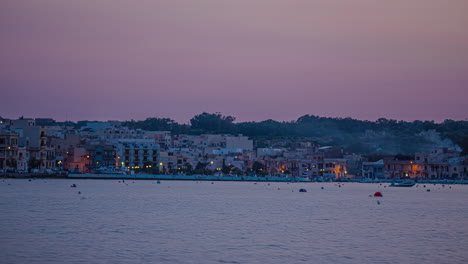 Puesta-De-Sol,-Las-Luces-Se-Encienden-En-Las-Casas-De-La-Pequeña-Ciudad-De-Marsaxlokk-En-Malta