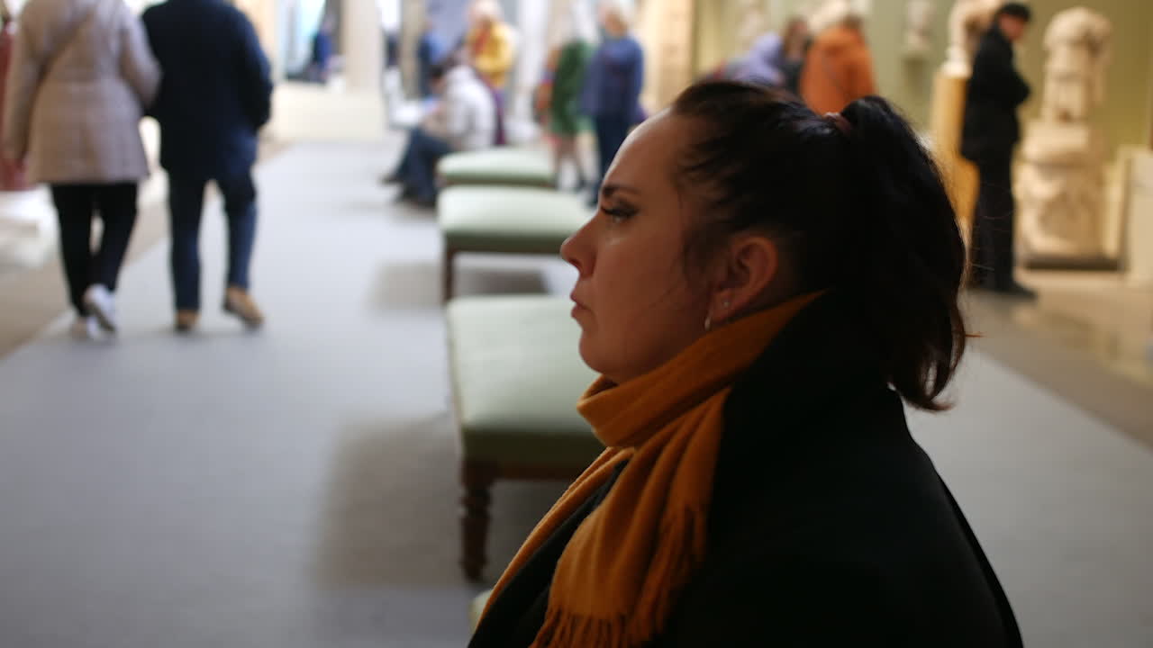 Una donna seduta in una galleria affollata di un museo che osserva una mostra.