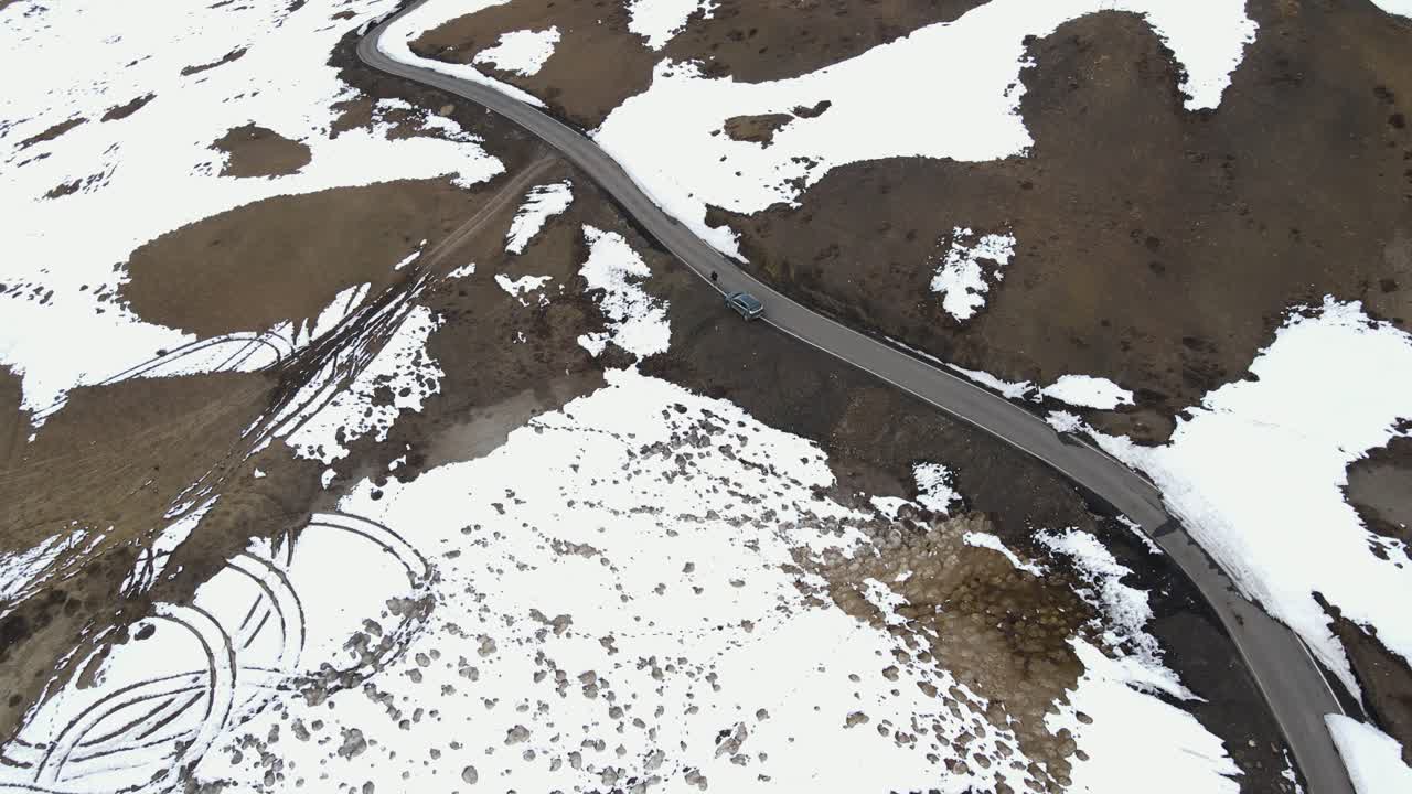 aerial view of snowy ice high mountains road with car driving on world's highest village hikkim in spiti valley in himachal pradesh