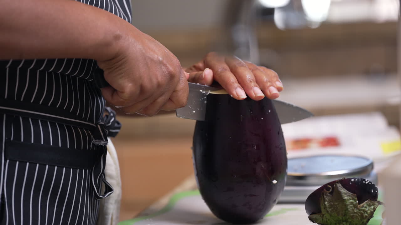 Black, African American hands slicing a large, whole eggplant in half - isolated slow motion