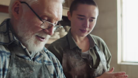 elderly sculptor giving lesson to young woman in workshop