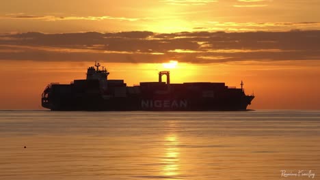 a majestic container ship silhouetted against a stunning sunrise over calm waters, capturing the beauty of maritime life and nature's splendor