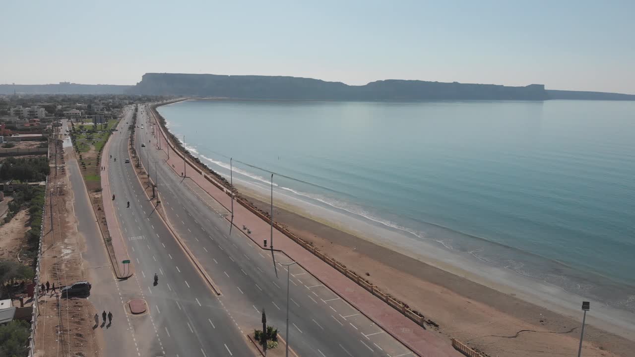 dolly aéreo justo sobre marine drive junto a la costa de la playa en gwadar con tráfico pasando