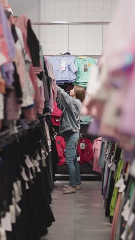 la mujer elige ropa para niños en la tienda. la dama en traje de vaqueros busca un traje elegante para niños en una gran tienda de moda. el cliente está en el pasillo entre los estantes