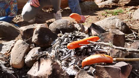 Sausages-deliciously-barbecued-and-moved-around-over-open-charcoal-camp-fire-using-carved-wooden-sticks