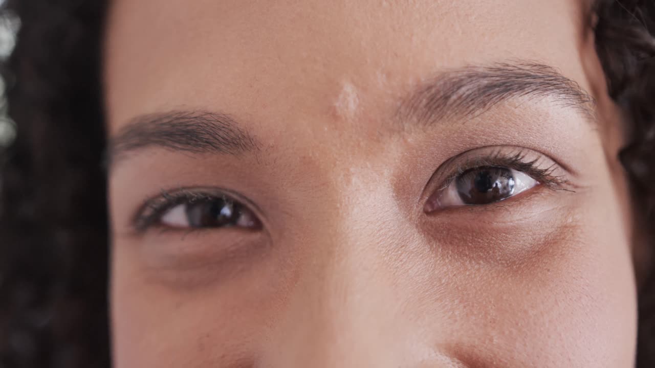 retrato de cerca de los ojos marrones de una mujer biracial feliz sonriendo en casa, en cámara lenta.