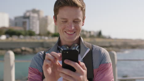 Retrato-De-Un-Atractivo-Joven-Pelirrojo-Usando-Un-Teléfono-Inteligente-En-La-Soleada-Playa-Enviando-Mensajes-De-Texto-Navegando-Por-Las-Redes-Sociales