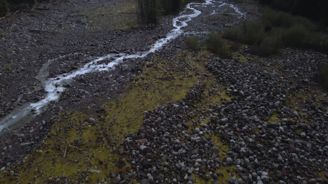 Aerial drone shot flying above a rocky creek at Mount Rainier with mountains rising in the background