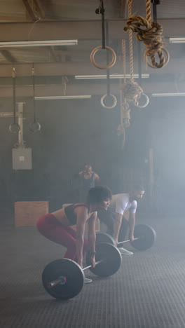 vertical video of diverse sports people lifting weight bars at gym in slow motion