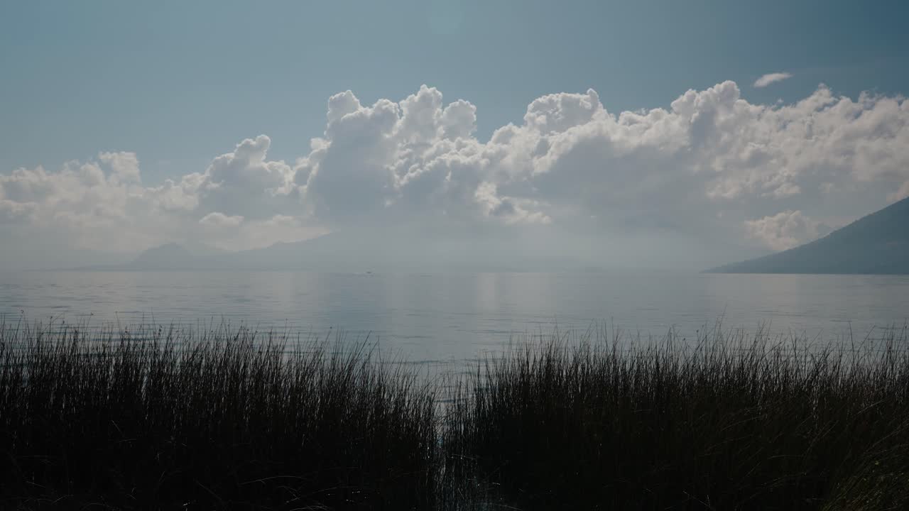 Calm Lake Atitlan reflects towering clouds above still water and reeds