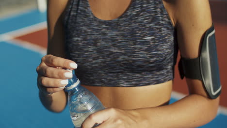 Close-Up-Of-A-Sporty-Woman-Standing-At-An-Outdoor-Court,-Resting-And-Drinking-Cold-Water-After-Workout